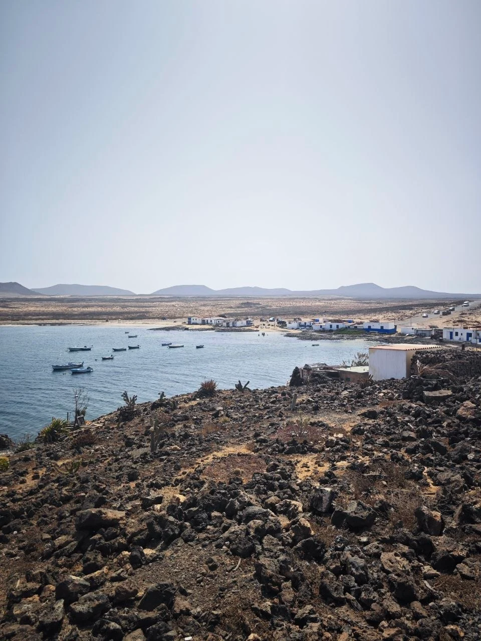 Fishing boats in the harbour of Ajuy, white houses behind a field of black lava and cacti
