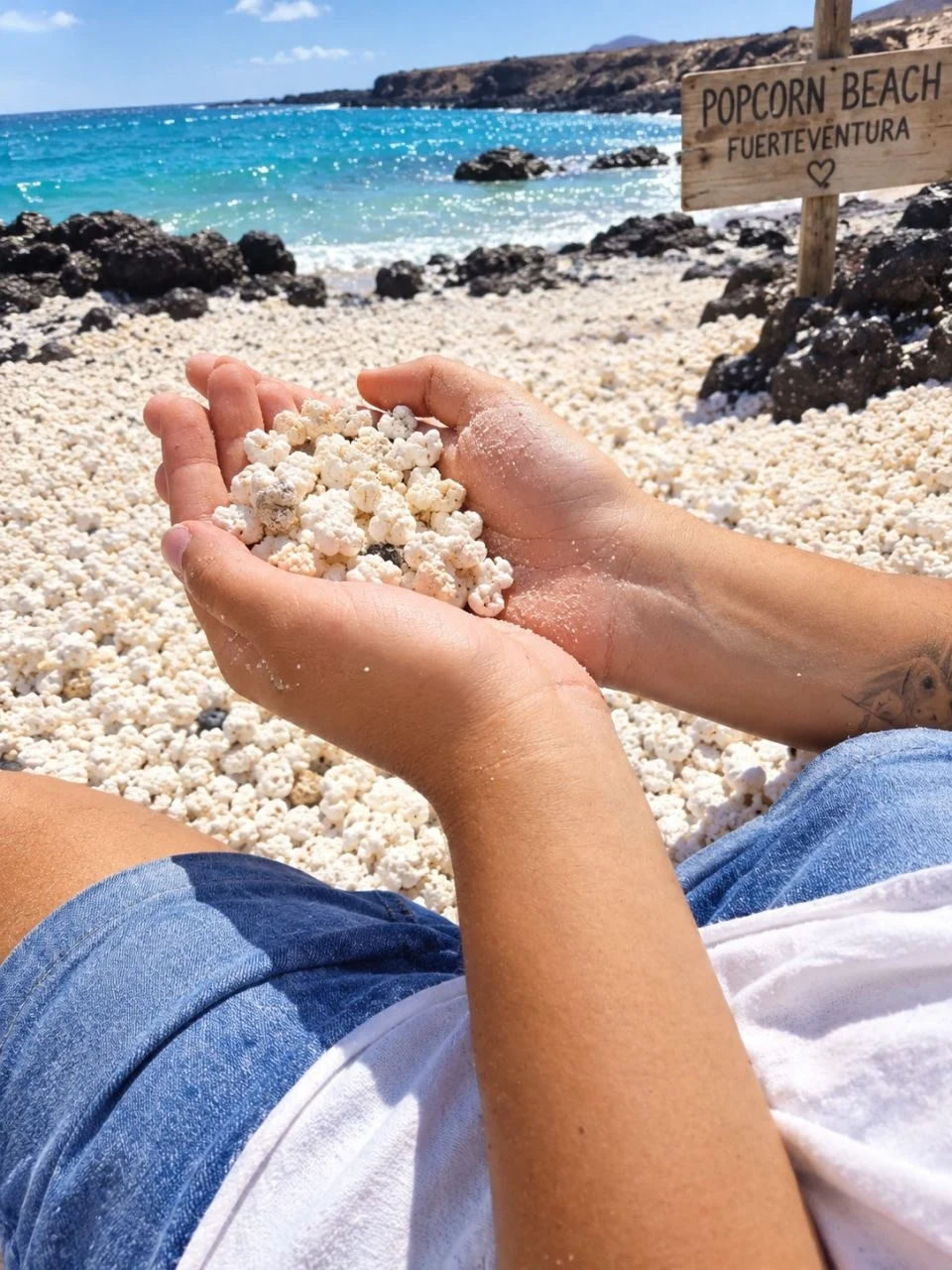 Hands holding white popcorn stones on Playa del Burro beside the turquoise sea