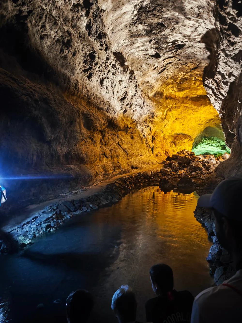 Inside a volcanic cave, golden light on the rock walls and a still green pool below