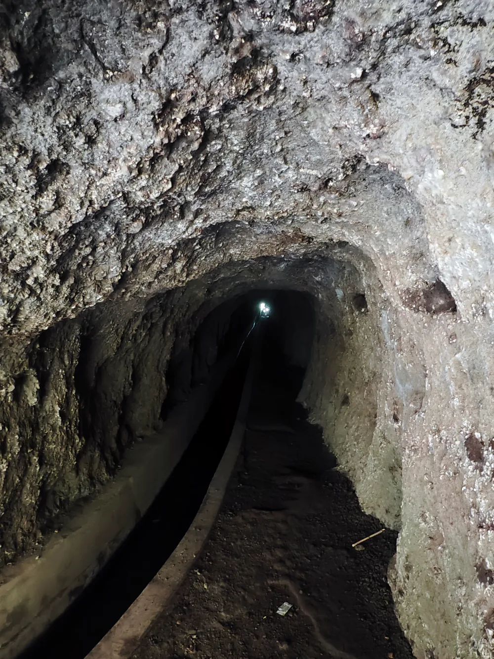 A single headlamp far down a dark lava tunnel on the Pico Ruivo ridge