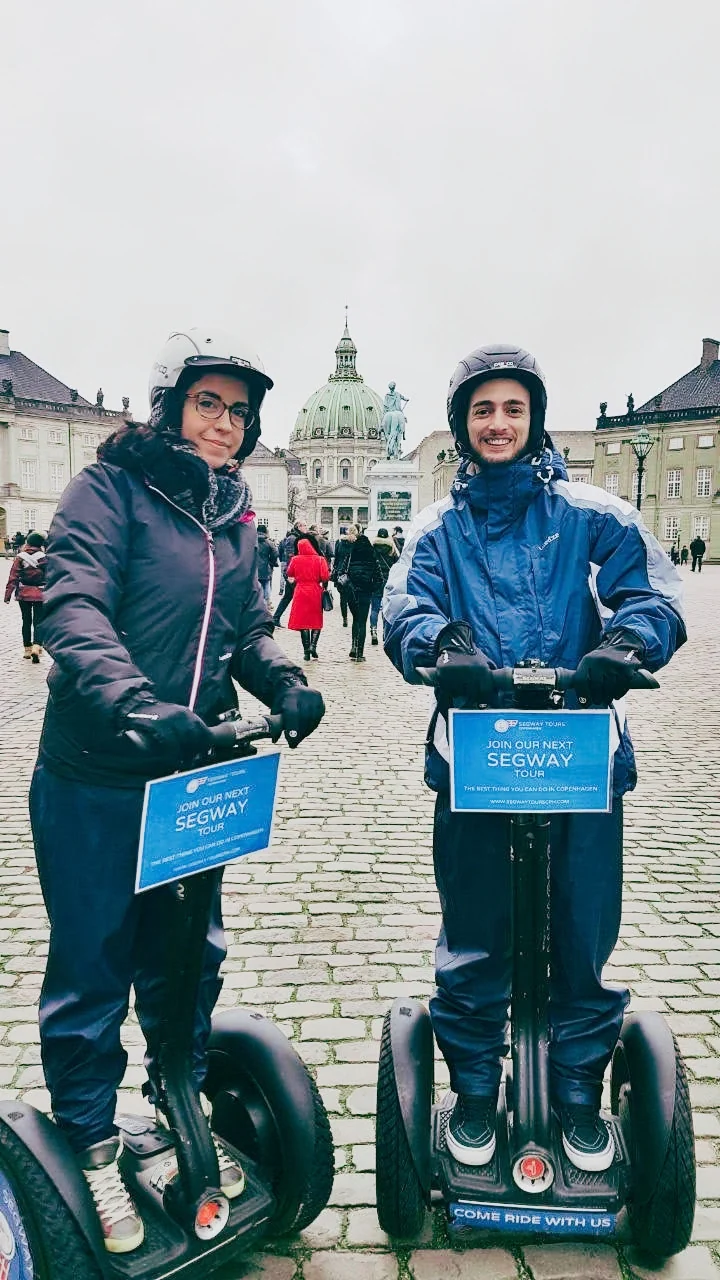 Valentina and Ivan in helmets standing on Segways in a city